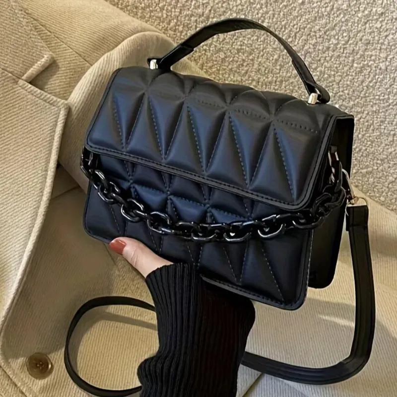 Bolso negro acolchado con cadena negra y correa larga, sostenido con una mano.
